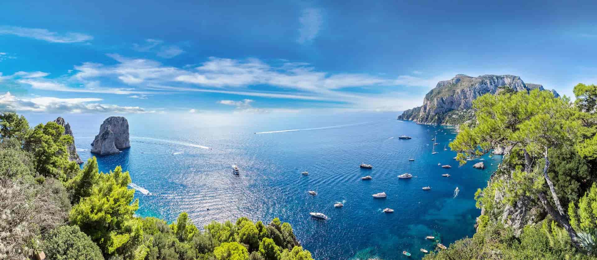 Boats on blue sea near rocky cliffs and green foliage, Capri Island.
