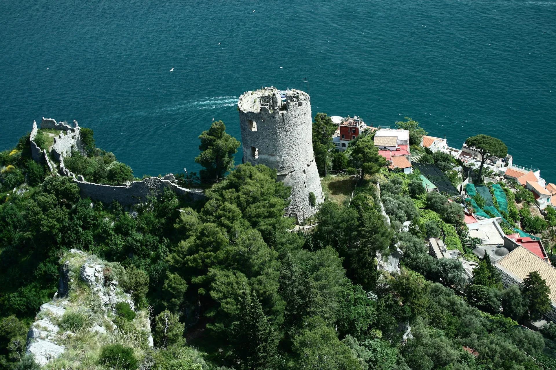 Torre dello Zirro ruins on a lush green cliff overlooking deep blue sea water.