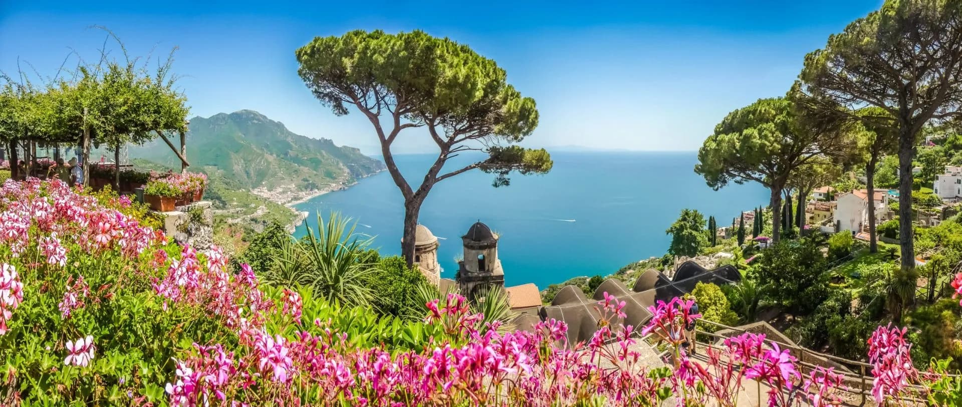 Terraced garden with pink flowers overlooking the blue sea and coastal town.