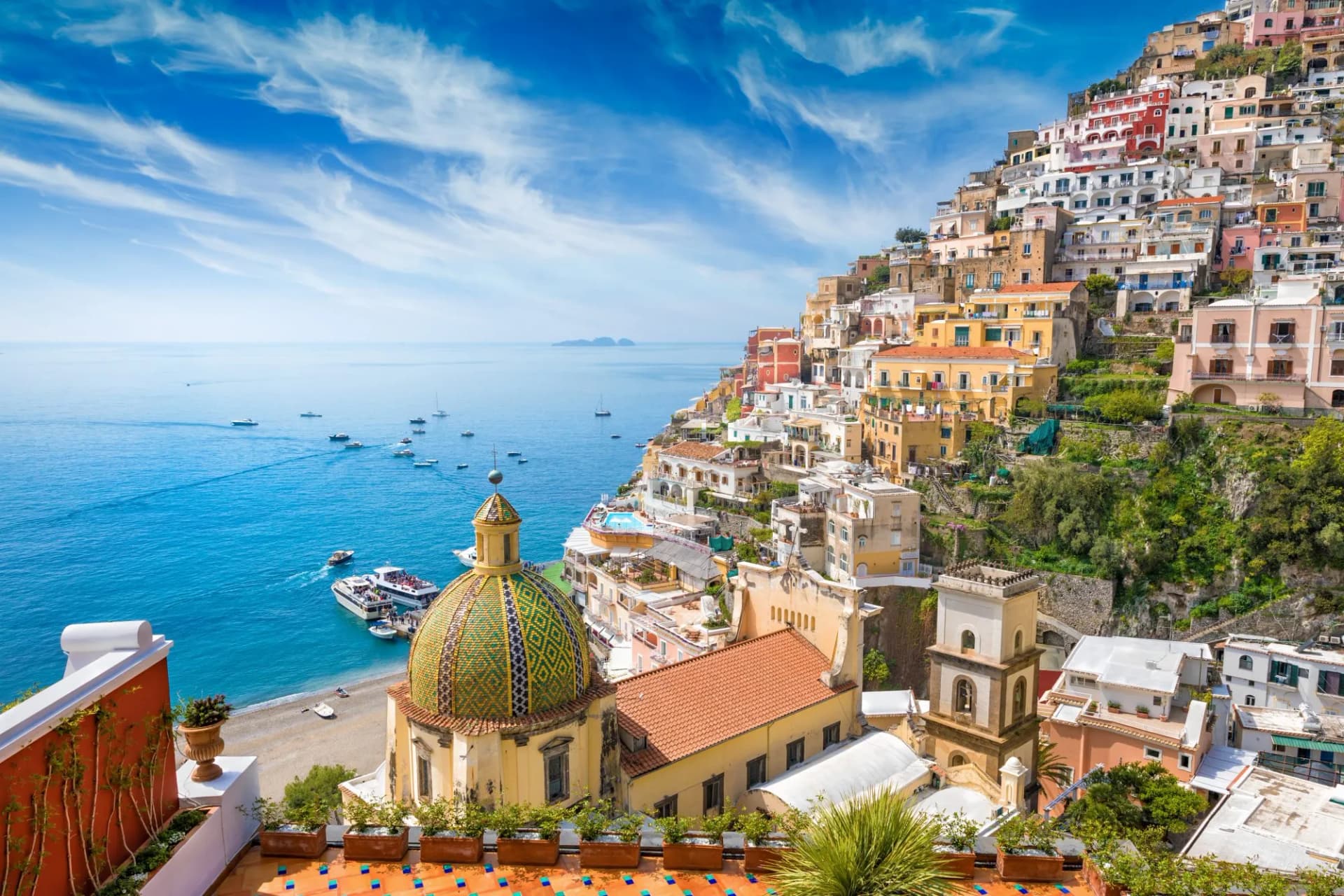 Colorful houses cascade down cliffside to the sea with boats in Positano, Italy.
