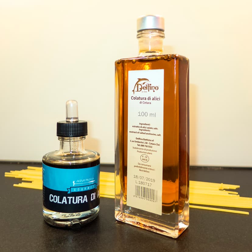 Bottles of Colatura di alici di Cetara anchovy extract with raw spaghetti pasta on a counter