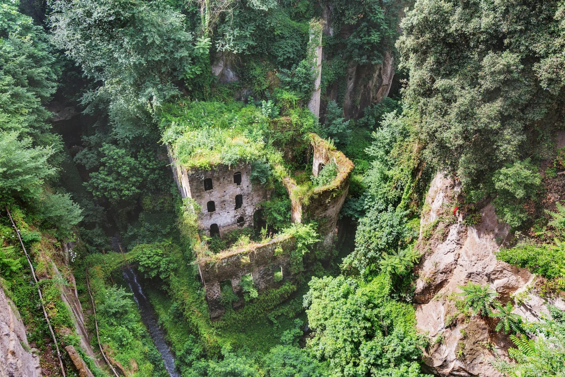 Ruins of Valle dei Mulini in Sorrento surrounded by dense green vegetation and steep cliffs.
