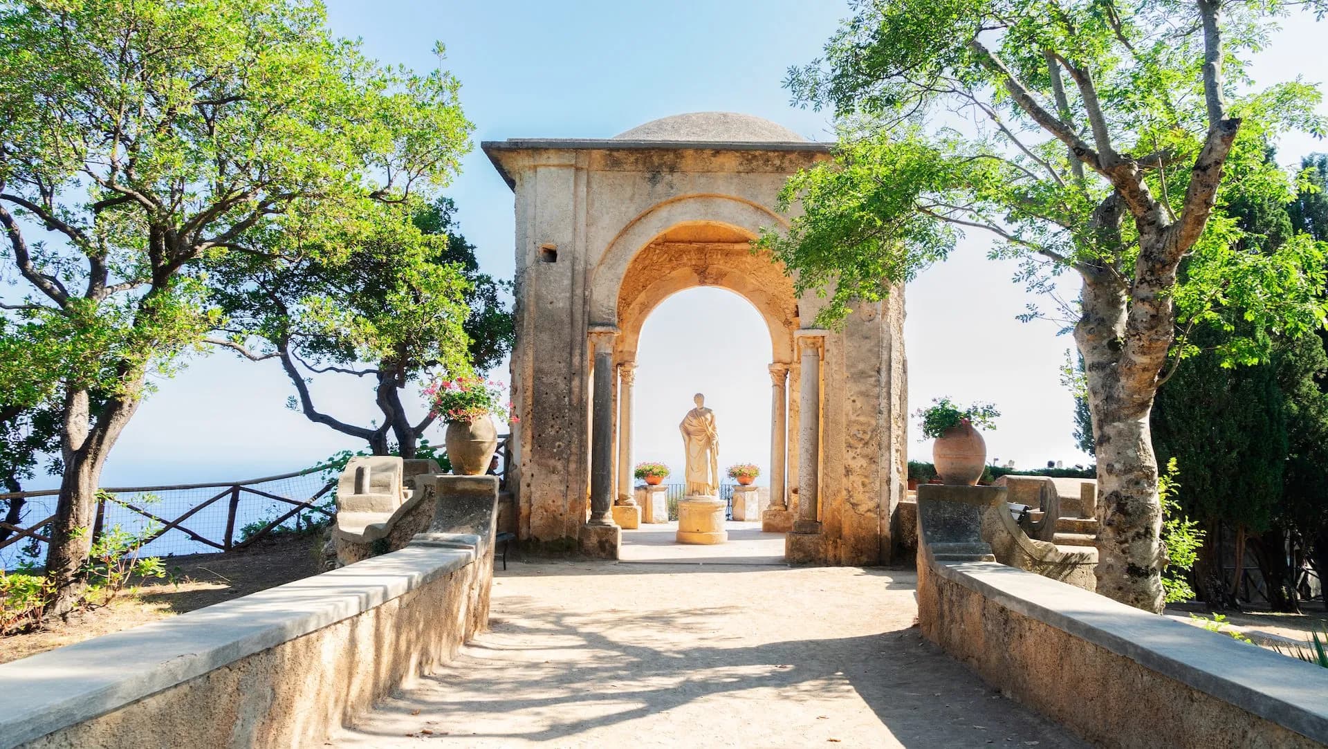 Stone archway with statue overlooking the sea, framed by trees in Ravello gardens.