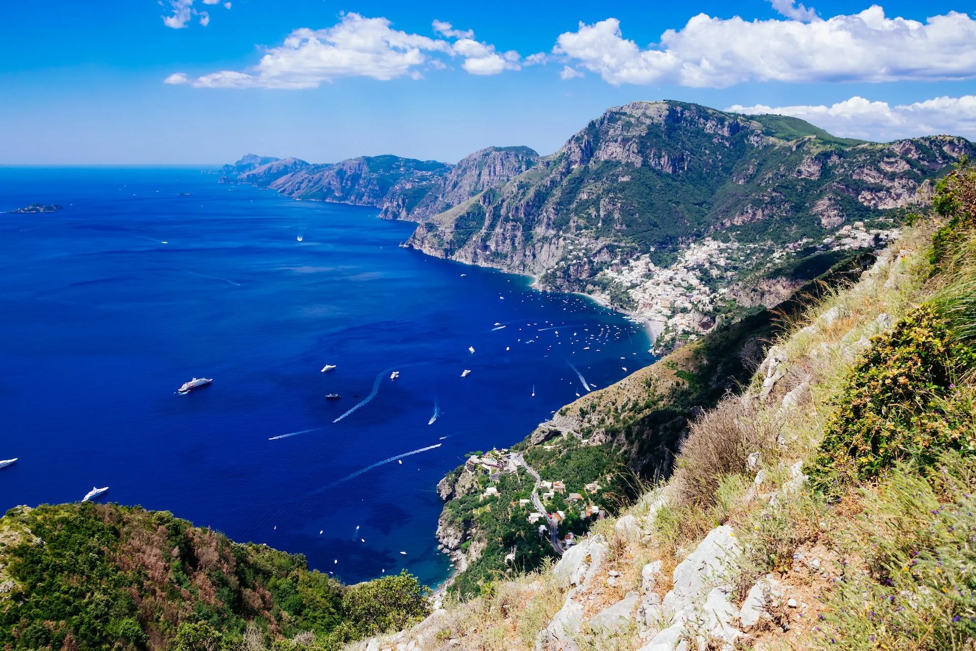 Hiking view of Positano and Amalfi Coast from Sentiero degli Dei above blue sea with boats.