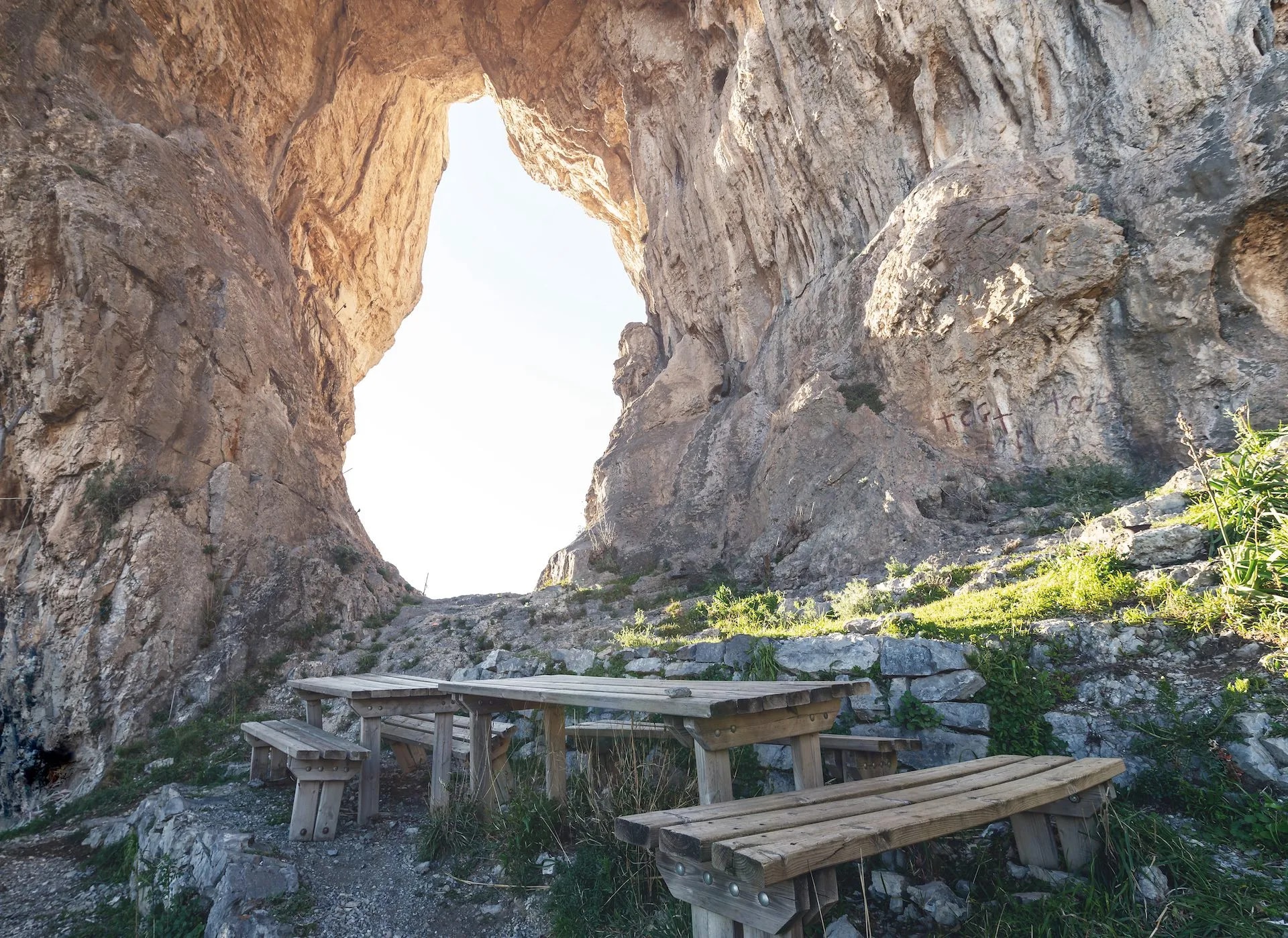 Picnic tables under a natural rock arch with bright light shining through the opening.