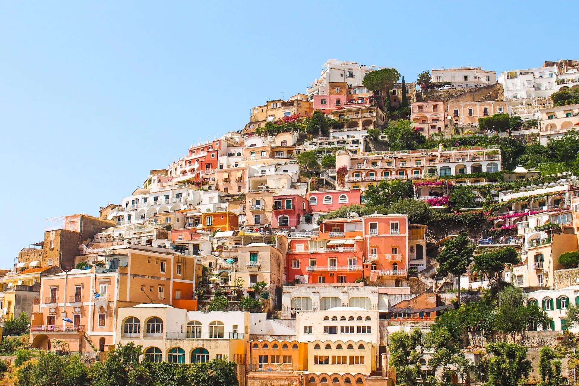 Colourful tiered Italian houses built into a steep hillside under a clear blue sky in Positano.