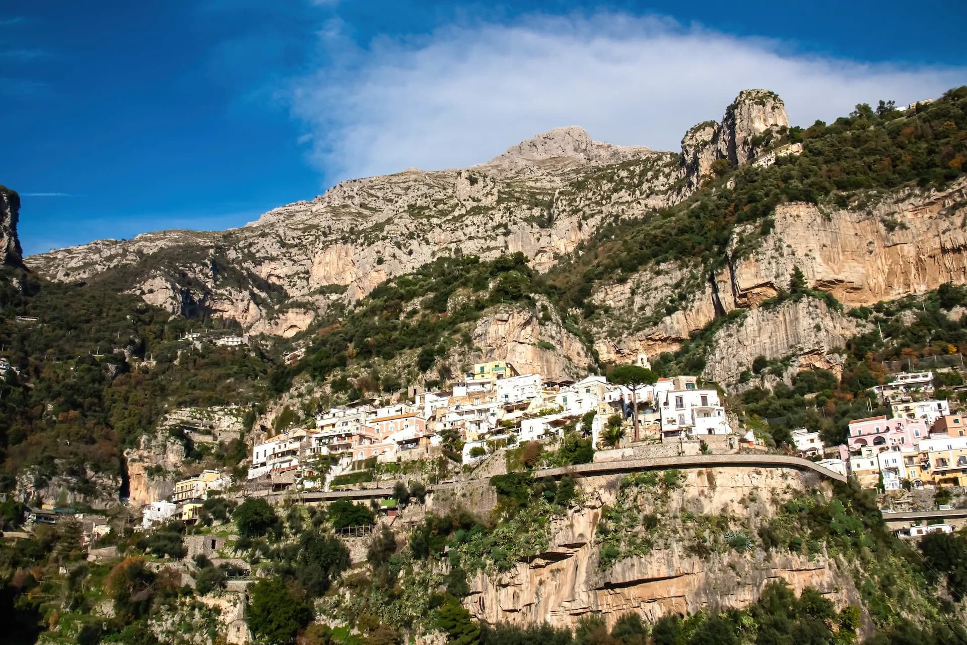 Coastal town Positano built into steep cliffs below Monte San Michele peaks under blue sky.