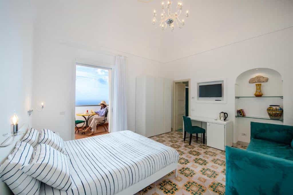 Bright hotel room with striped bedding, balcony access, and sea view in Albadamare.