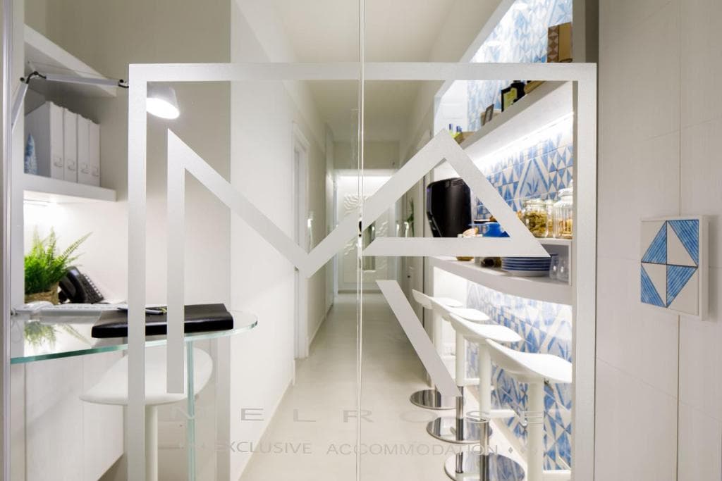 Modern interior with white bar stools, blue patterned tiles, and "MelRose" logo on glass door.
