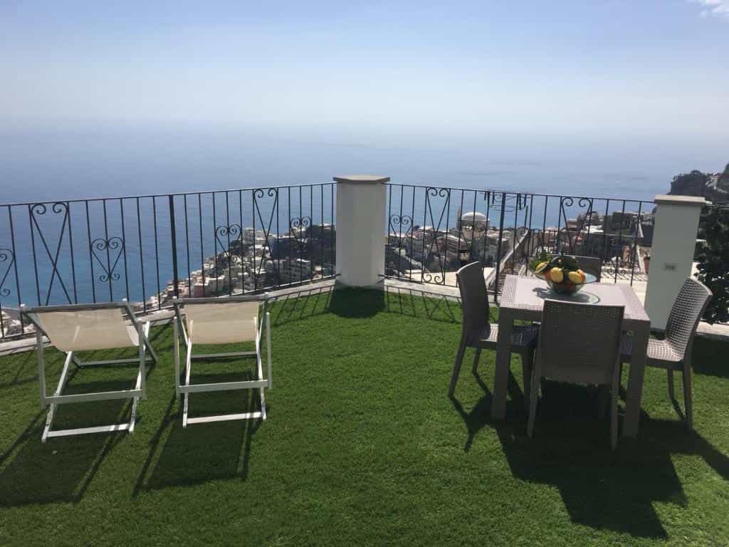 Terrace with artificial grass, lounge chairs, and dining set overlooking Mediterranean coastal town and sea.