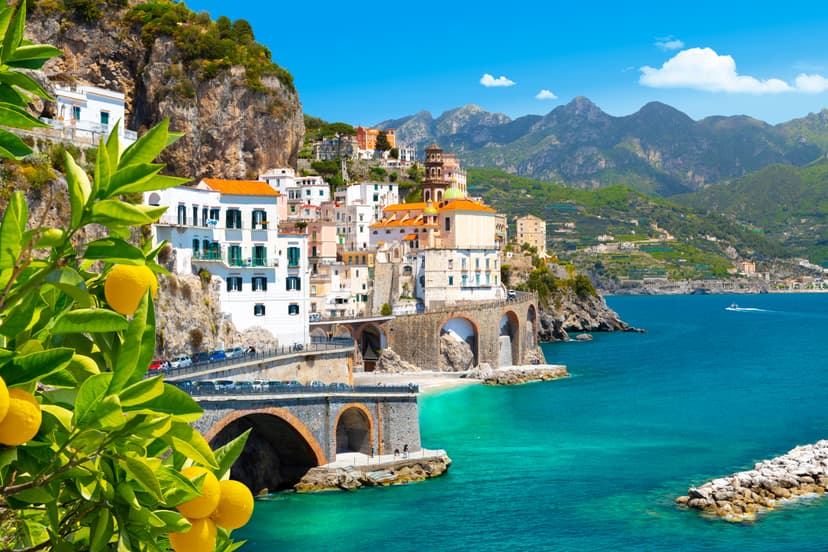 Lemon branch frames colorful buildings on cliffside above turquoise sea in Atrani, Amalfi Coast.