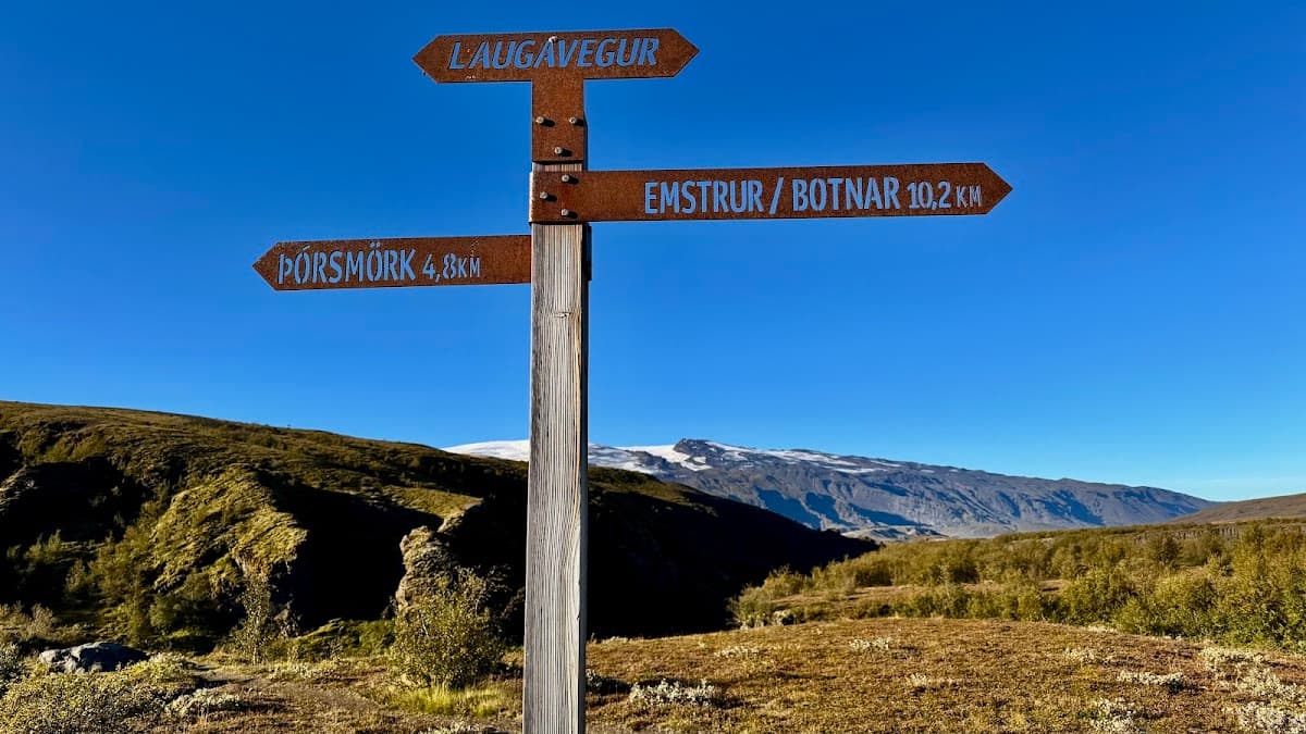 Hiking trail sign with directions to Laugavegur, ΓΓ³rsmΓΆrk, and Emstrur against a mountainous landscape and blue sky